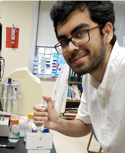 a young man with dark hair and a beard wearing glasses in a lab