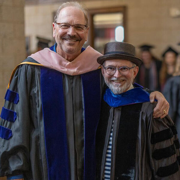 two male professors in academic robes smile at the camera