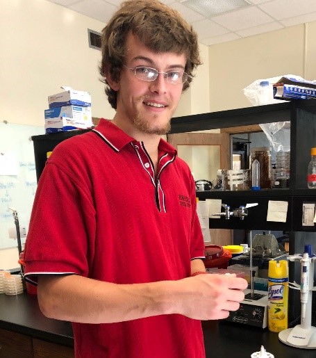 a young man in a red shirt and glasses stands in a lab