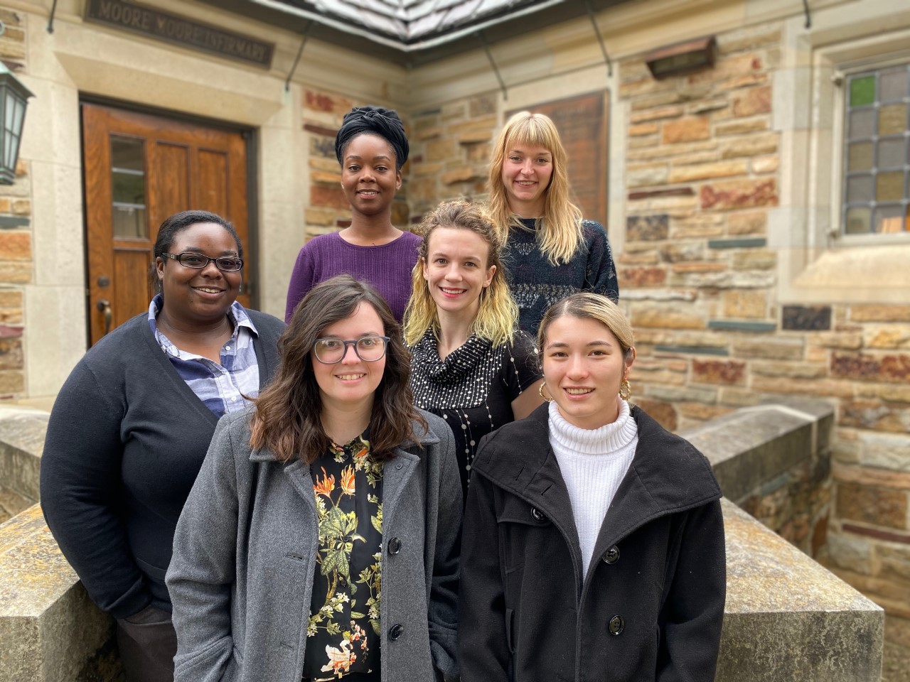 six women stand in front of a stone building