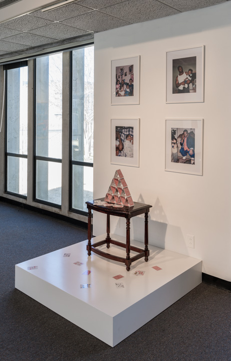Installation with table, house of cards, and photographs. 