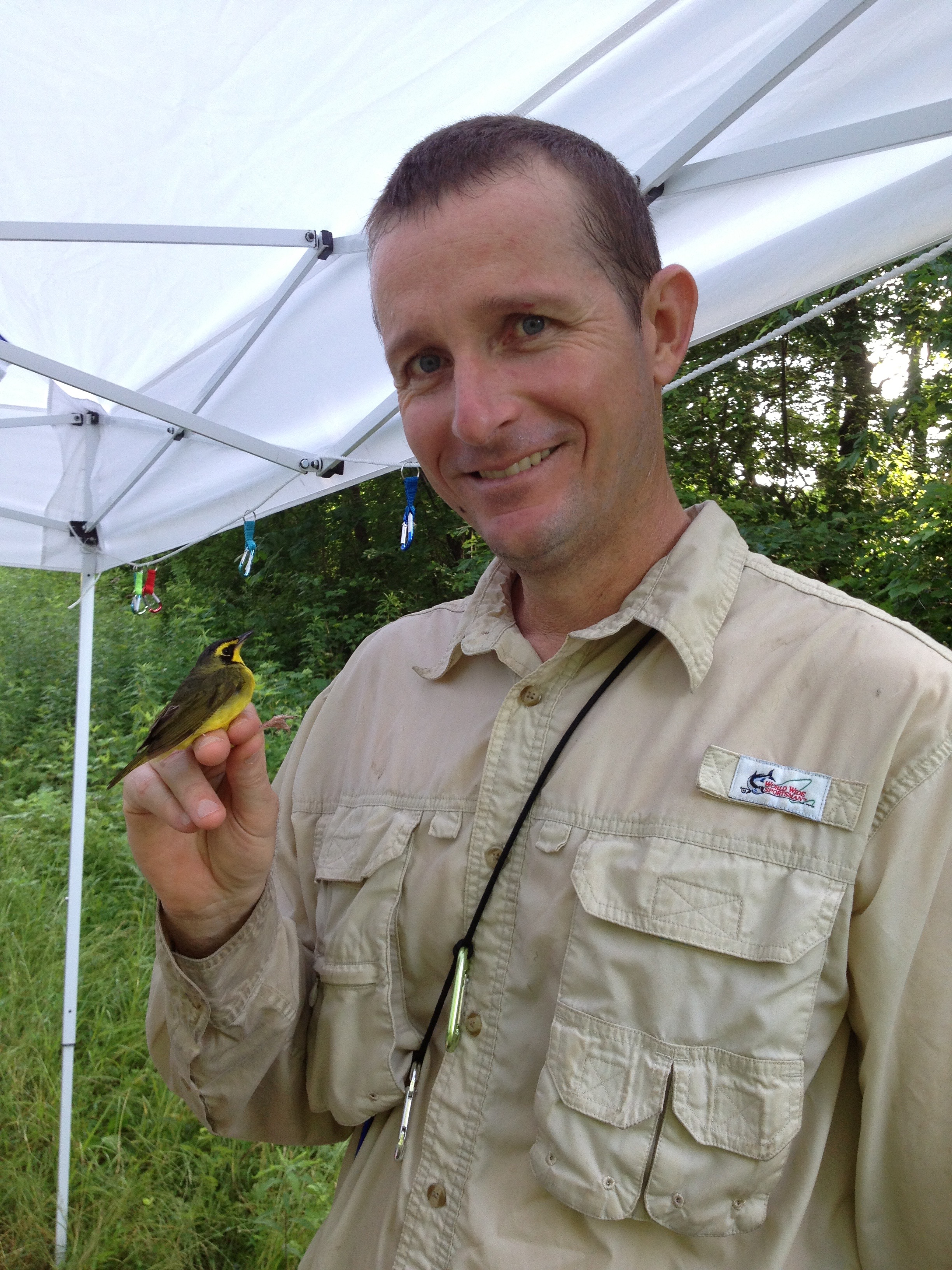 a man holds a small bird in his hand and smiles at the camera