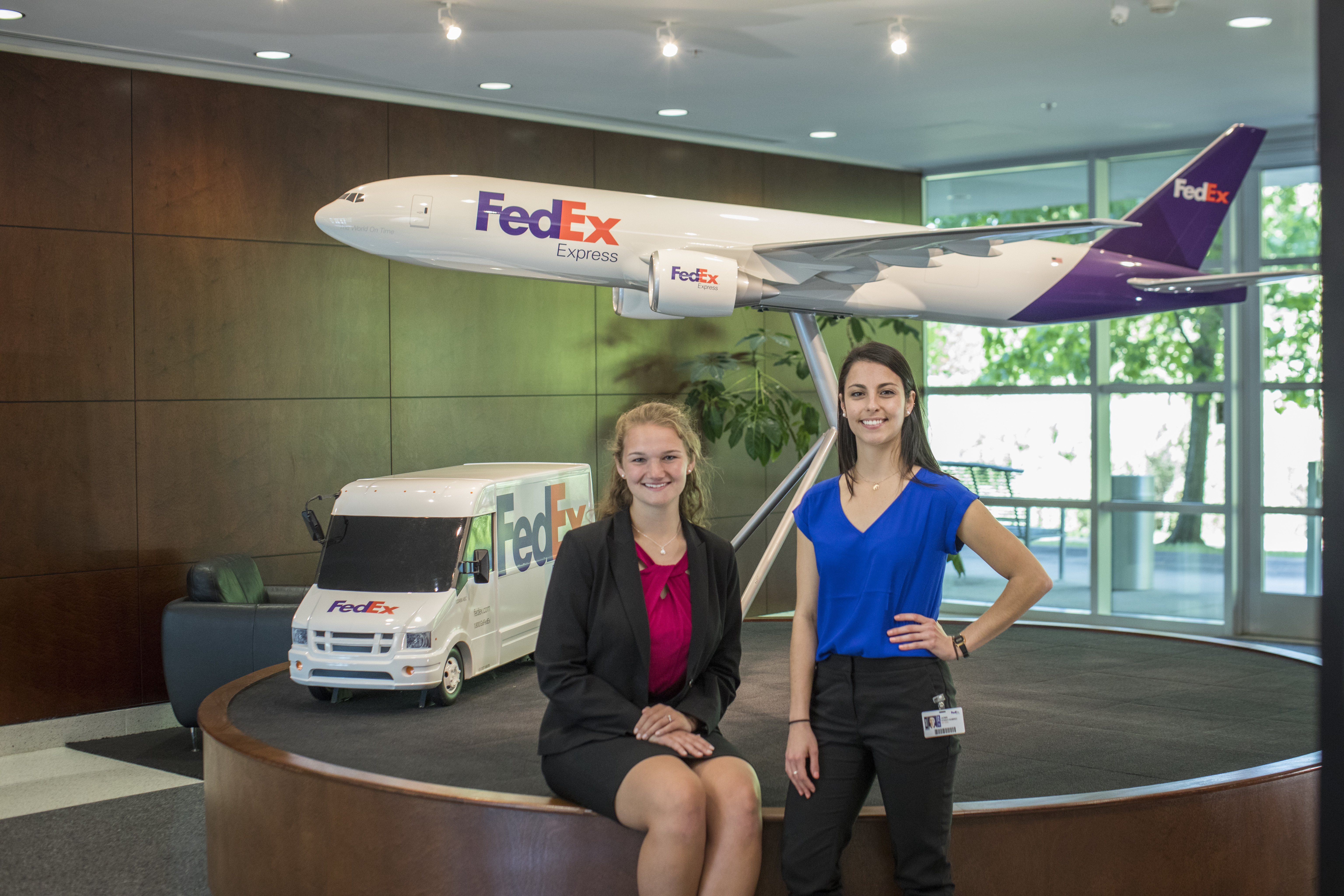 two young women stand in front of a model of a FedEx plane