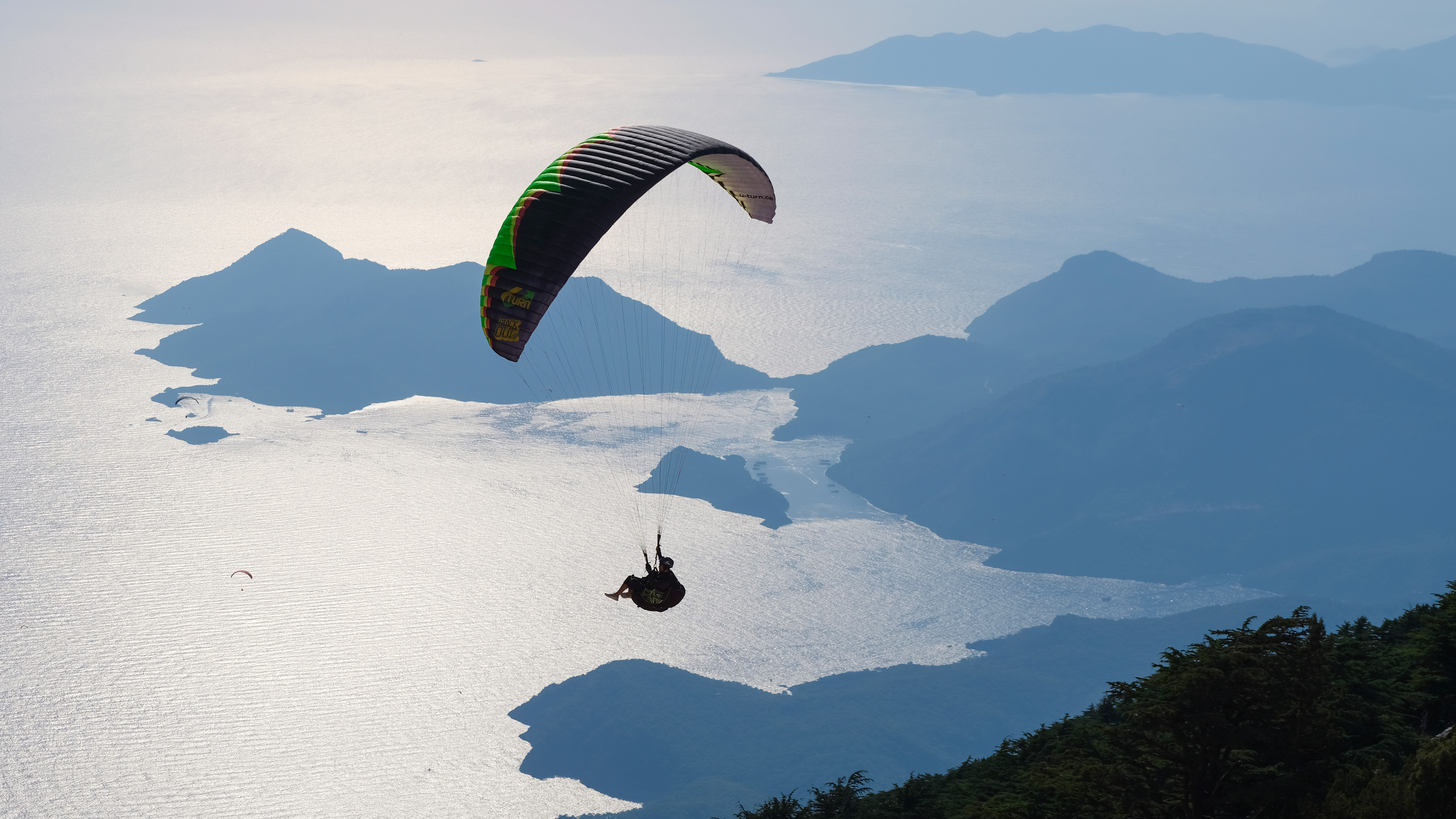 A person parachuting over an oceanside mountain range. 