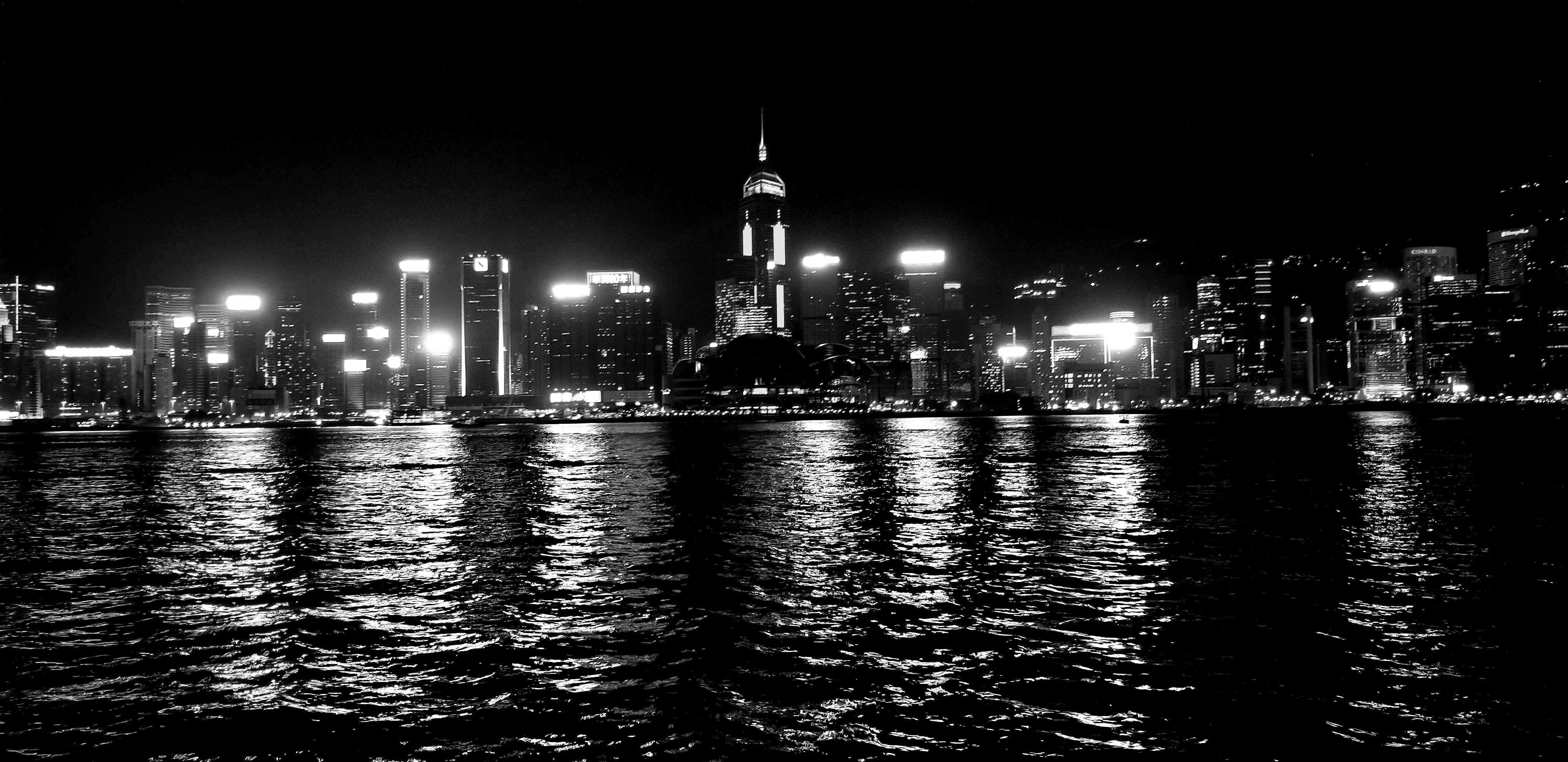 Black and white photo of a city at night, taken from on the water. 