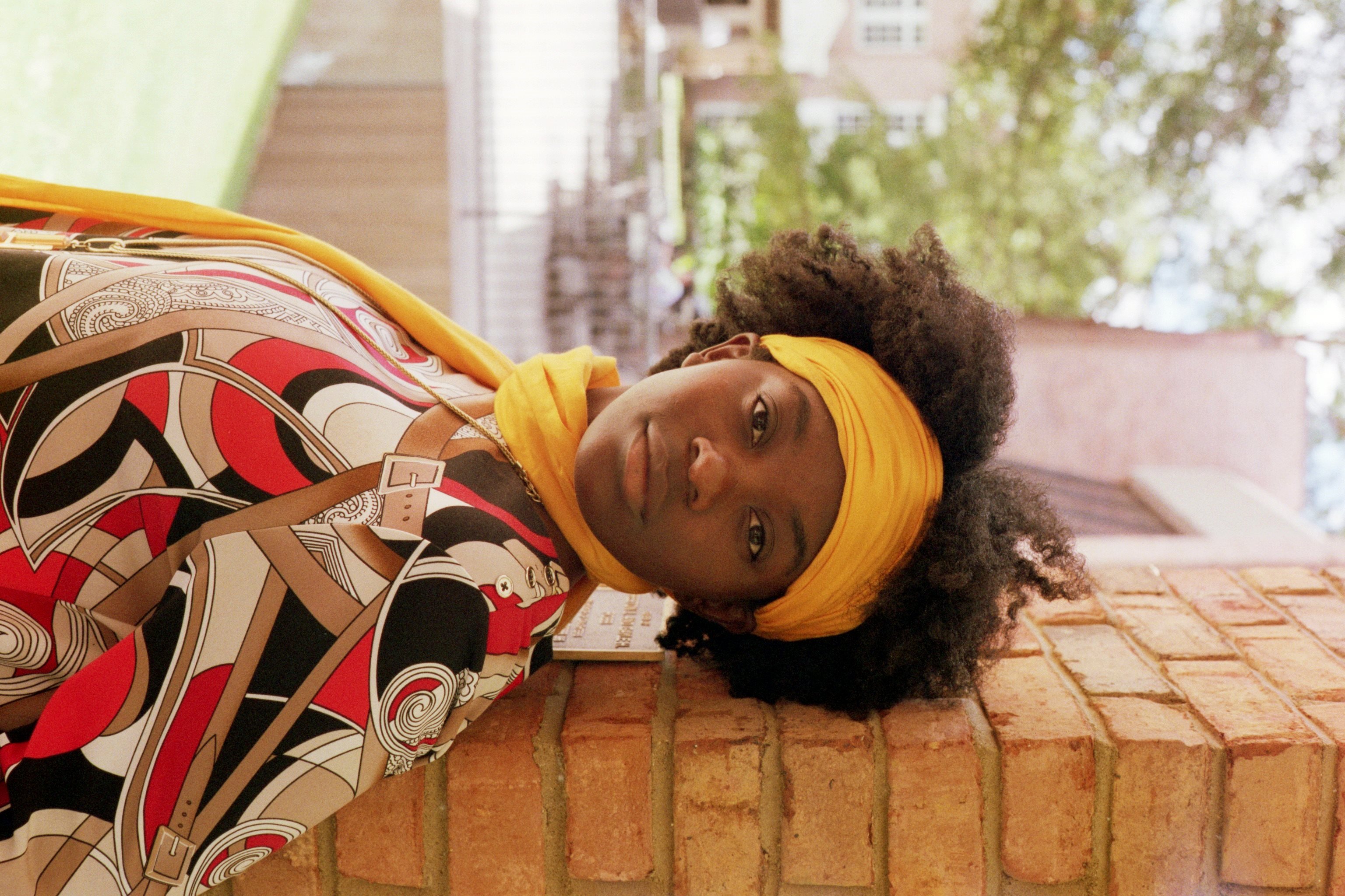 A woman in a yellow bandana standing against a brick wall