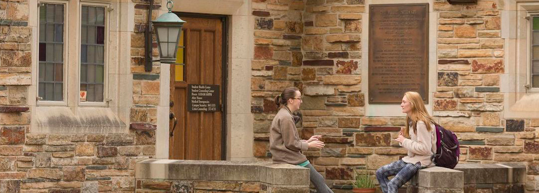 students sit on steps in front of stone building