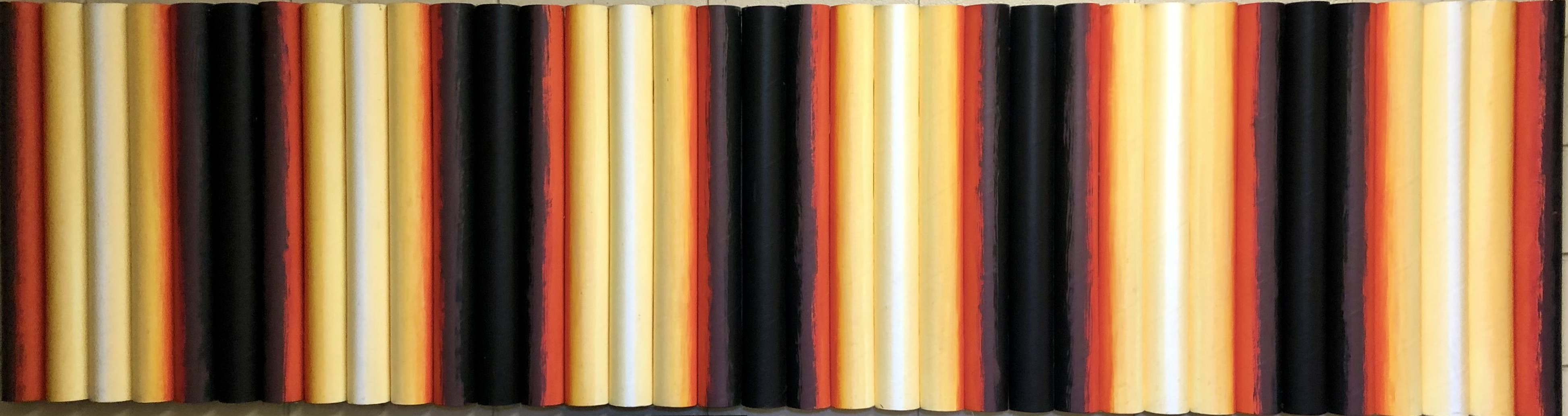 Vertical yellow, red, white, and black cardboard cylinders are positioned in a long horizontal line