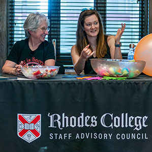 Two ladies sitting at a table, speaking and gesturing. The tablecloth says, "Rhodes College Staff Advisory Council."