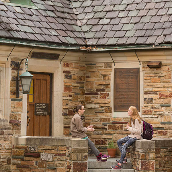 students chat on the steps of a Gothic stone building