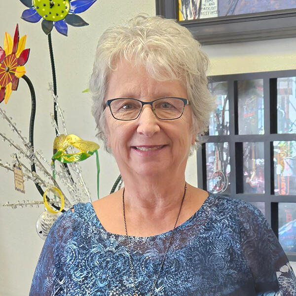 a woman in glasses stands before a window and flowers