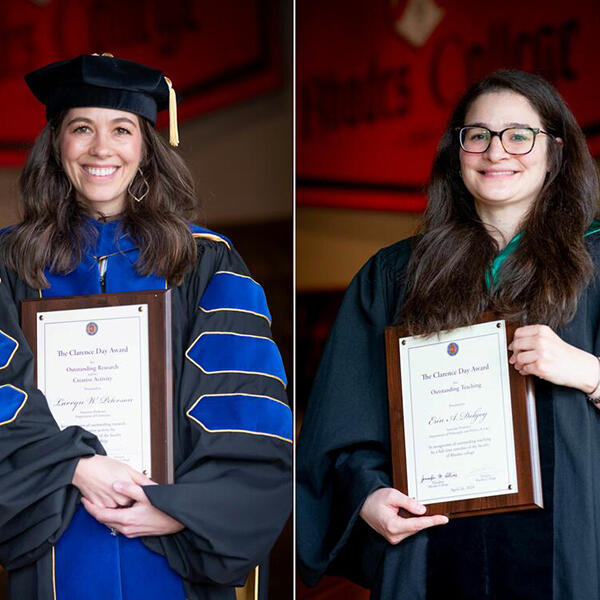 two women in academic robes holding award plaques