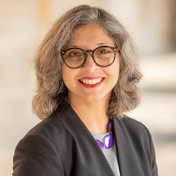 a woman with glasses and wavy hair smiles at the camera