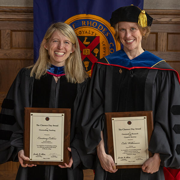 two women in academic robes holding award plaques