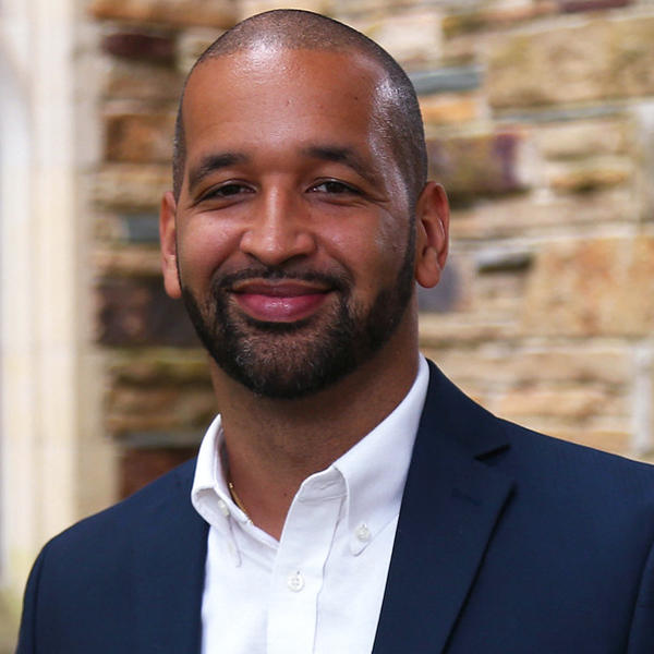 an African American man in a blue suit jacket smiles at the camera